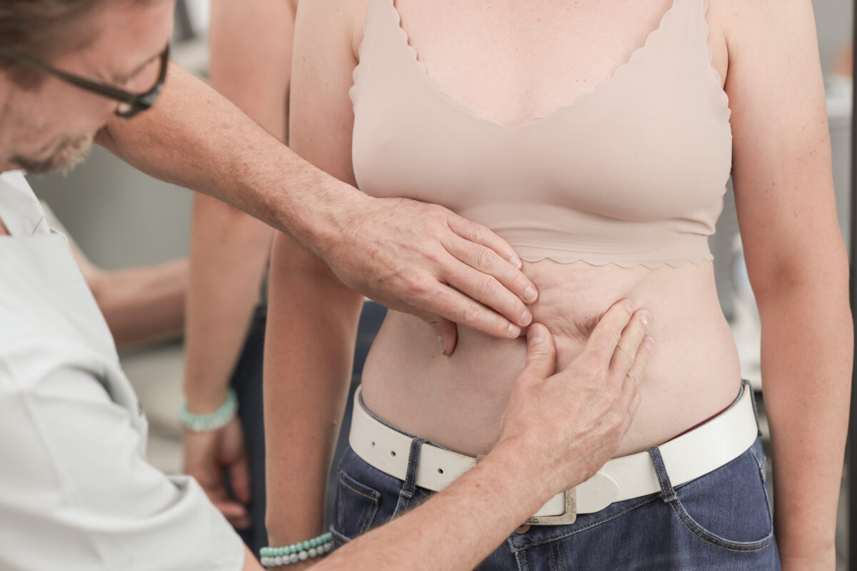 Plastmed Arzt tastet Haut an Bauch bei Frau ab