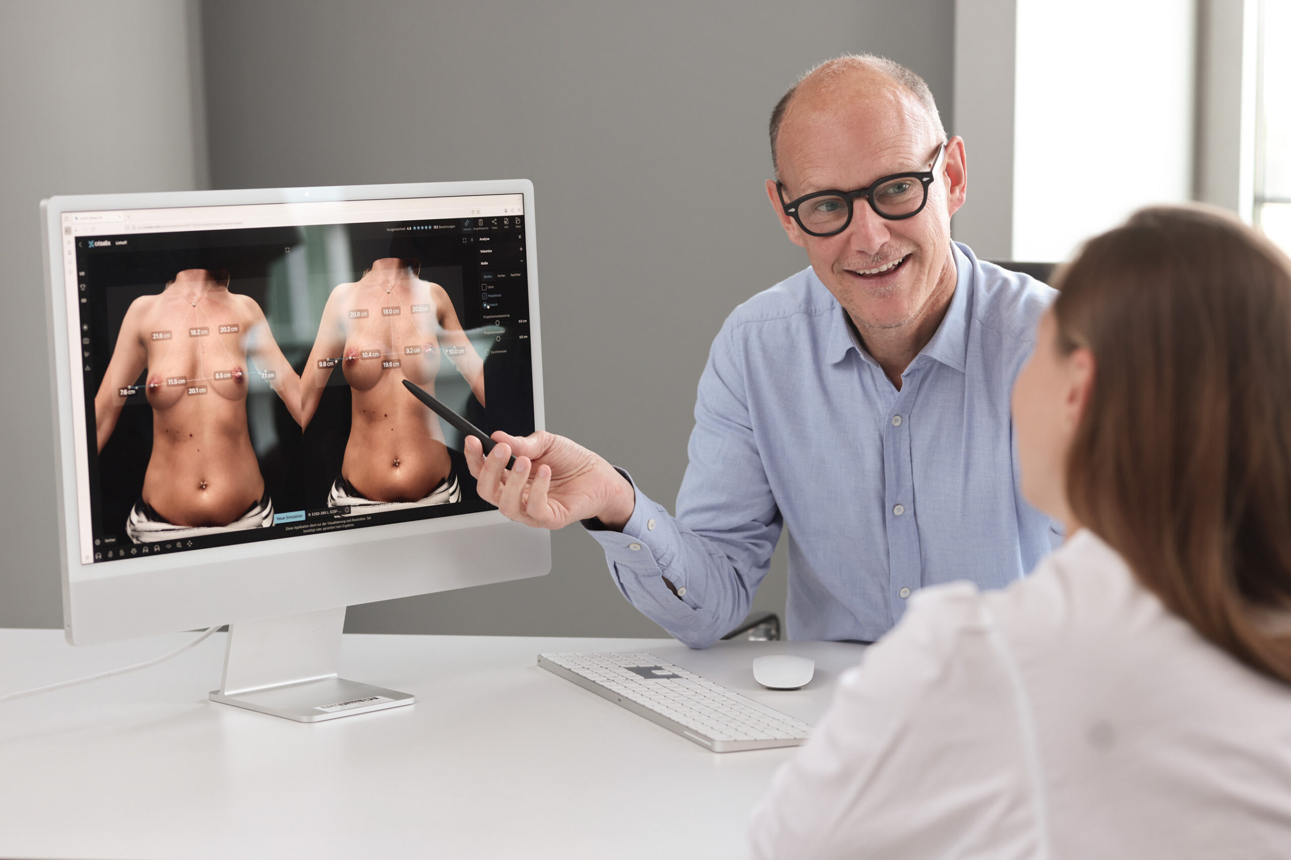 Frau ist beim Erstgespräch für eine Brustvergrößerung, -verkleinerung oder Entfernung von Implantaten bei Plastmed Düsseldorf, durchgeführt von Dr. med. Till Scholz, der eine Simulation des Resultats am Computer zeigt