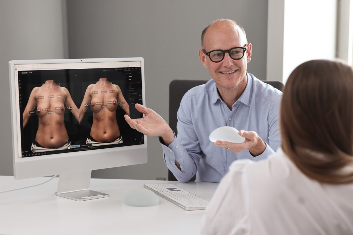 Frau ist beim Erstgespräch für eine Brustvergrößerung oder Entfernung von Implantaten bei Plastmed Düsseldorf, durchgeführt von Dr. med. Till Scholz, der eine Simulation des Resultats am Computer zeigt