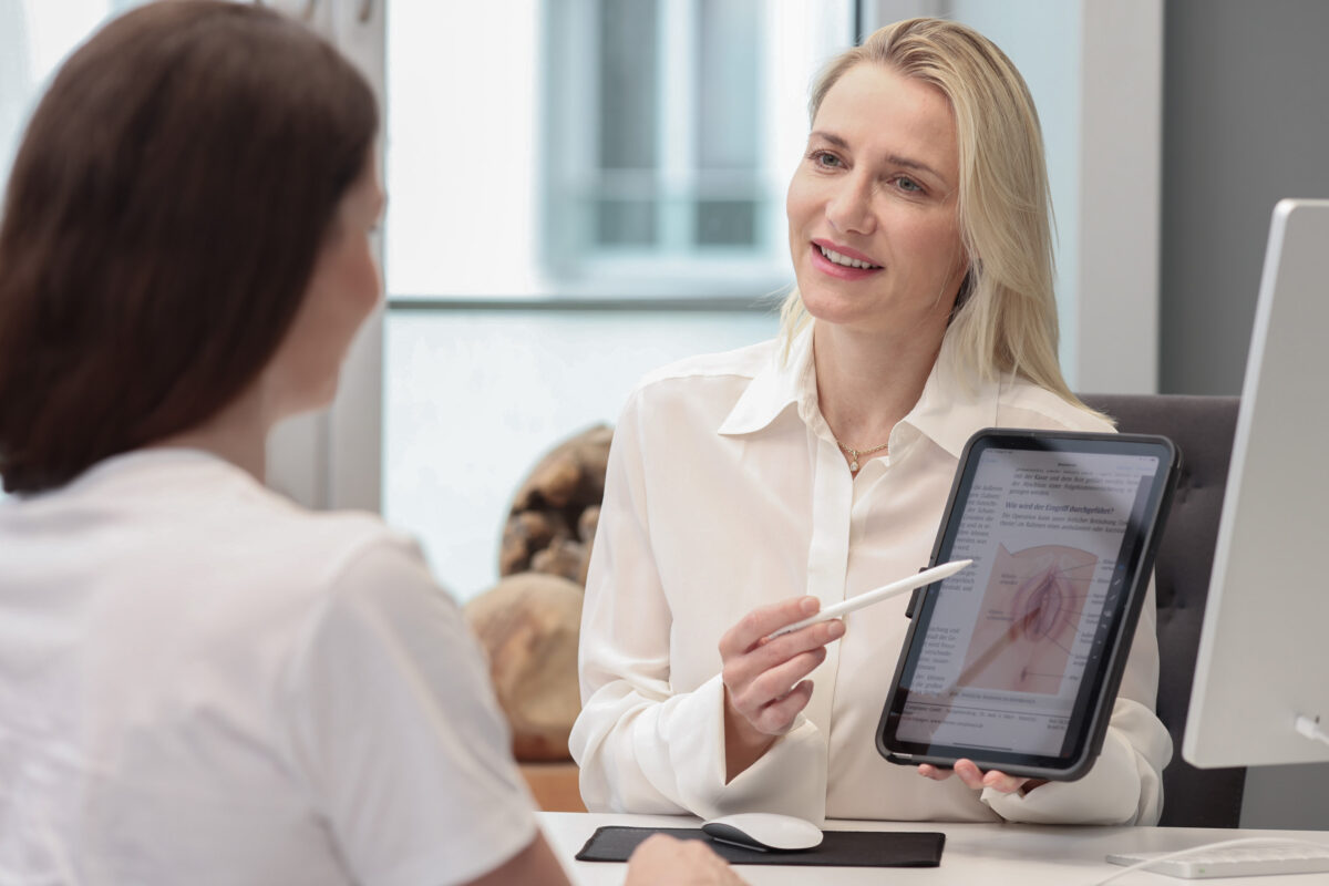 Frau ist beim Erstgespräch für eine intimchirurgische Bahandlung bei Plastmed Düsseldorf, durchgeführt von Dr. med. Naja-Norina Pluto, die auf einem Tablet Bilder des Eingriffs zeigt