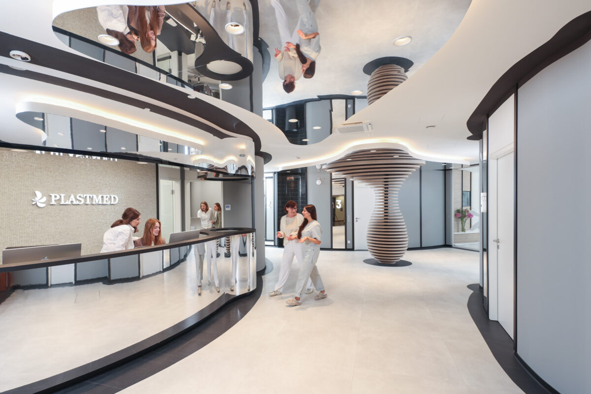 Empfang und Eingangsbereich mit Skulptur in der Plastmed Privatklinik in Düsseldorf, zwei Ärzte unterhalten sich und man sieht Mitarbeiter am Empfang