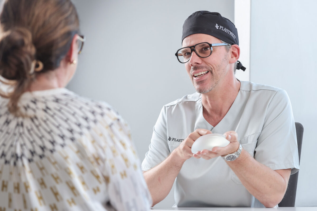 Frau ist beim Erstgespräch für eine Brustvergrößerung, -verkleinerung oder Entfernung von Implantaten bei Plastmed Düsseldorf, durchgeführt von Dr. med. Jens Diedrichson, der ein Silikonimplantat in der Hand hält