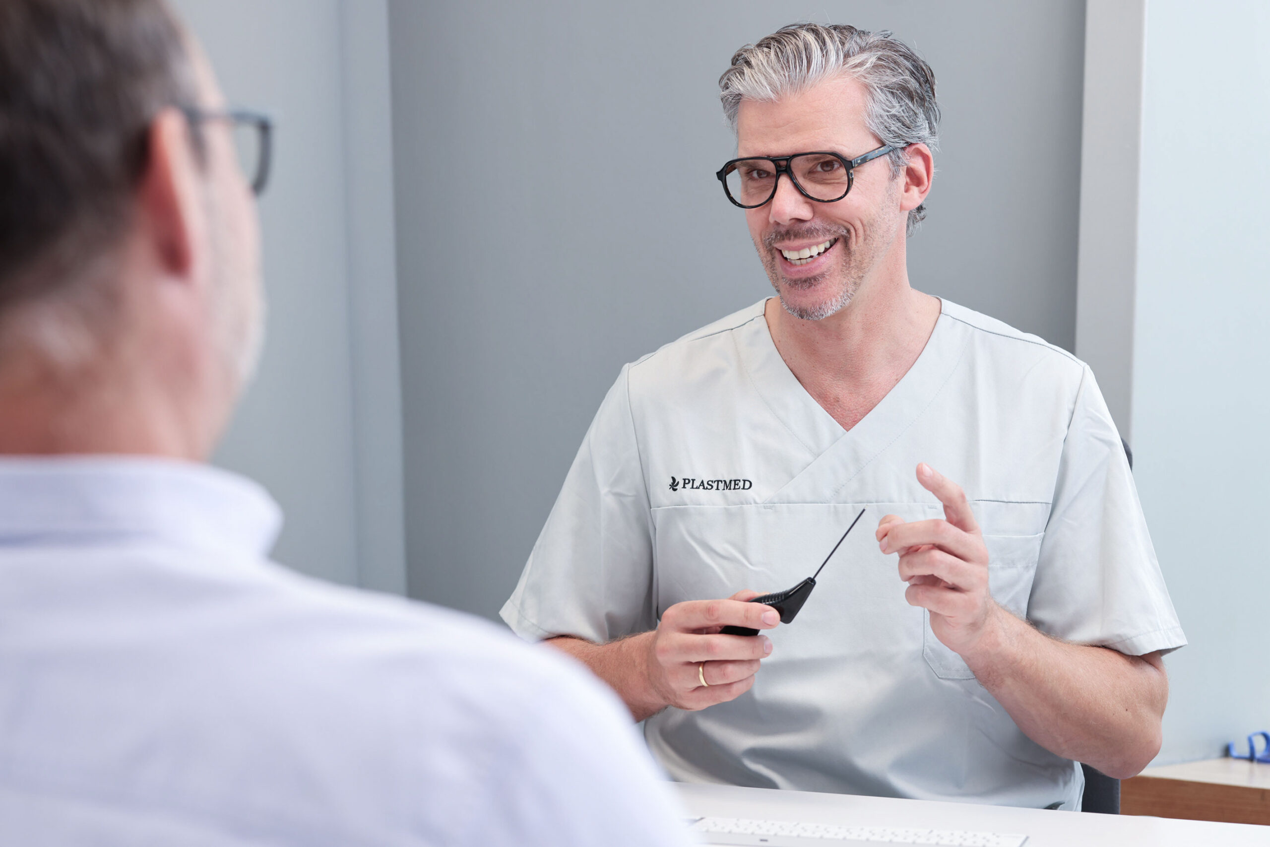 Mann wird von Dr. med. Jens Diedrichson zur Radiofrequenz-Behandlung beraten, der ein medizinisches Gerät in der Hand hält.